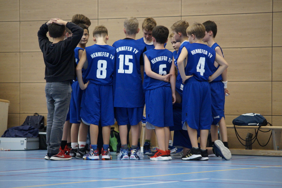 Gruppe von Jungen in blauen Basketballtrikots versammelt sich um einen Trainer in einer Sporthalle.
