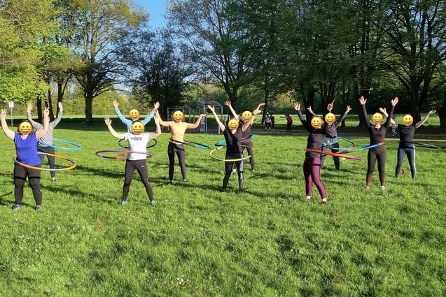 Gruppe von Personen mit Emoji-Gesichtsmasken, die fr&ouml;hlich Hula-Hoops in einem Park nutzen.