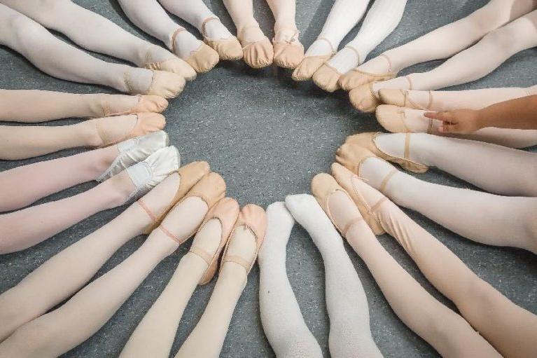 Kreis aus Ballettbeinen mit verschiedenen Tanzschuhen auf dem Boden, einige F&uuml;&szlig;e zeigen in die Mitte.