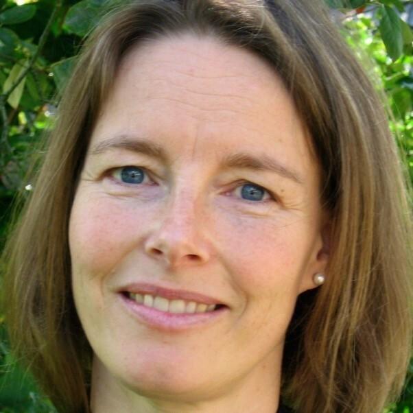 Frau mit kurzen, braunen Haaren und blauen Augen lächelt vor grünem Hintergrund. Sie trägt ein Ohrring.