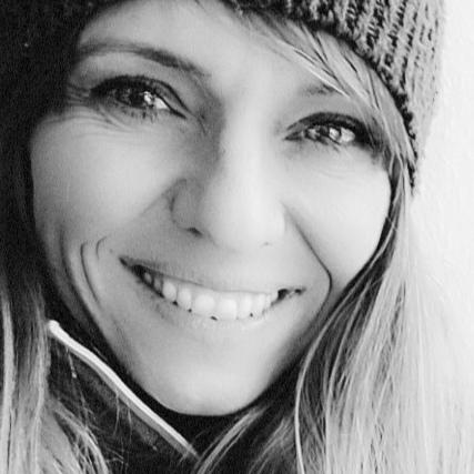 Porträt einer lächelnden Frau mit langen Haaren, die eine Mütze trägt, in schwarz-weiß.