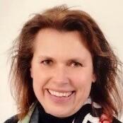 Portrait einer lächelnden Frau mit lockigem, schulterlangem Haar und einem bunten Schal um den Hals.