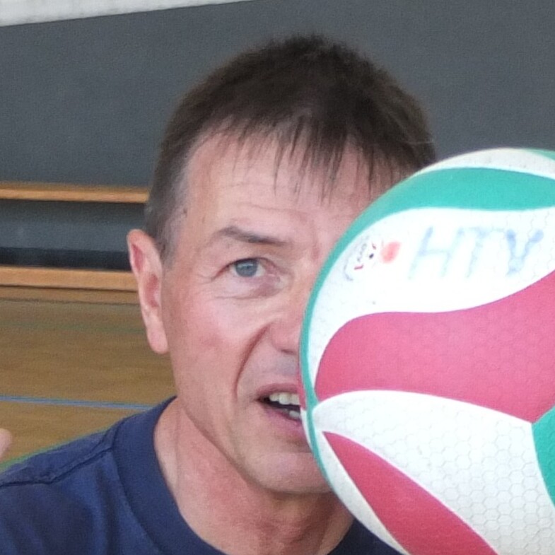 Mann h&auml;lt einen Volleyball vor seinem Gesicht, mit sichtbarem Netz im Hintergrund.