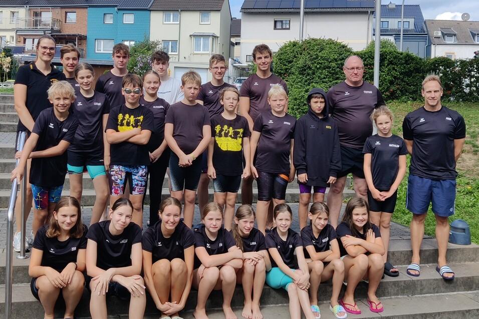 Gruppenfoto einer Schwimmmannschaft in sportlichen T-Shirts auf einer Treppe im Freien.