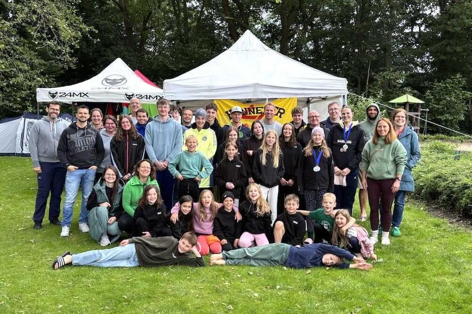Gruppenfoto einer Vielzahl von Personen, die vor einem Zelt im Freien stehen. Einige tragen Medaillen.