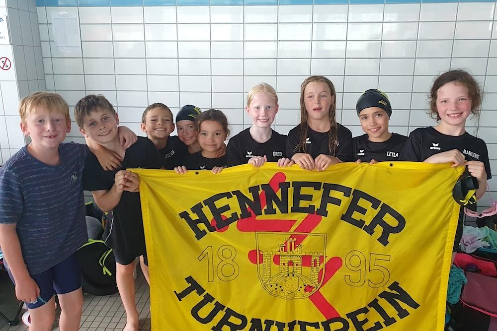 Gruppenfoto von acht Kindern in Schwimmbekleidung, die eine Fahne des Hennefer Turnvereins halten.
