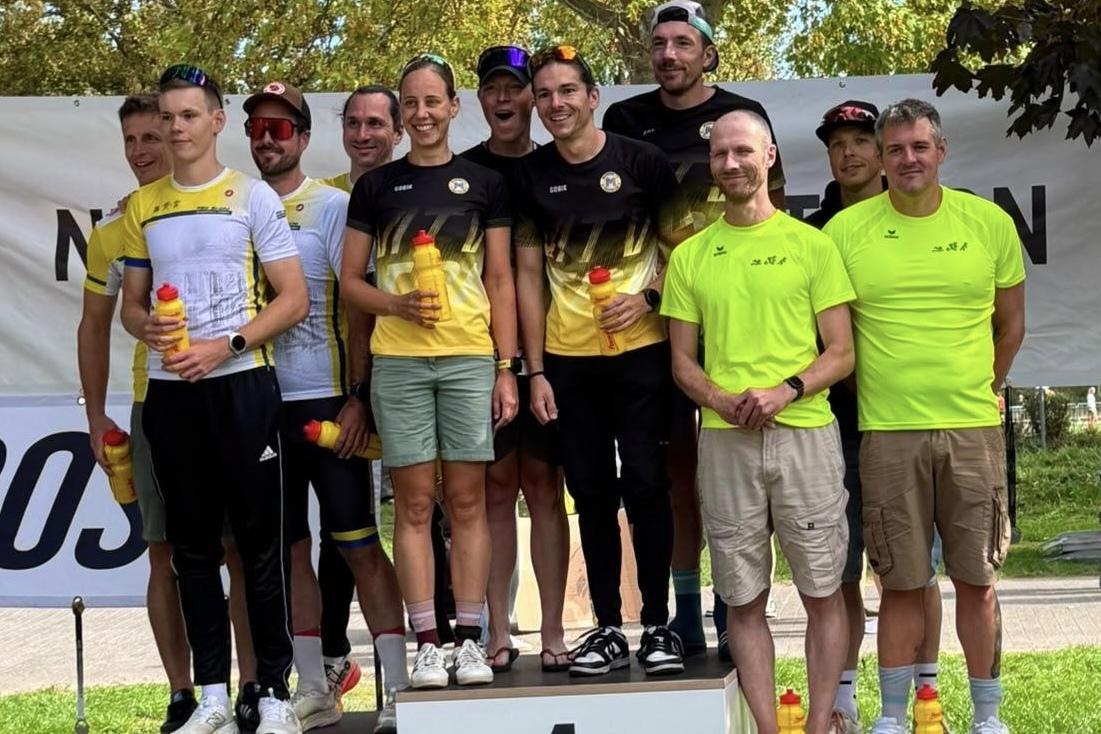 Gruppe von Sportlern auf dem Treppchen bei einer Siegerehrung, mit Medaillen und Getr&auml;nken in der Hand.