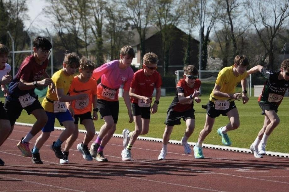 Gruppe von Jugendlichen startet beim Laufwettbewerb auf einer Leichtathletikbahn unter blauem Himmel.