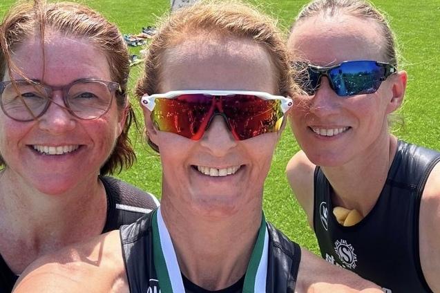 Drei Frauen in Sportkleidung l&auml;cheln in die Kamera, mit Sonnenbrillen und einer Medaille um den Hals, auf einem gr&uuml;nen Rasen.
