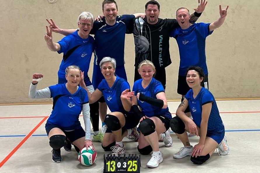 Gruppenselfie von acht Volleyballspielern in blauen Trikots, jubelnd vor einer Wand mit Punkteanzeige (13:25).