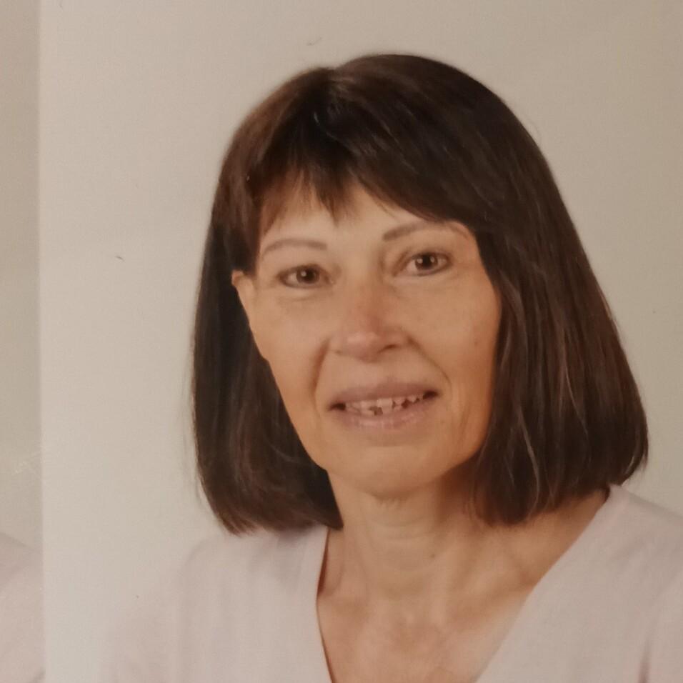 Porträt einer Frau mit schulterlangen braunen Haaren, die in die Kamera lächelt, vor hellem Hintergrund.