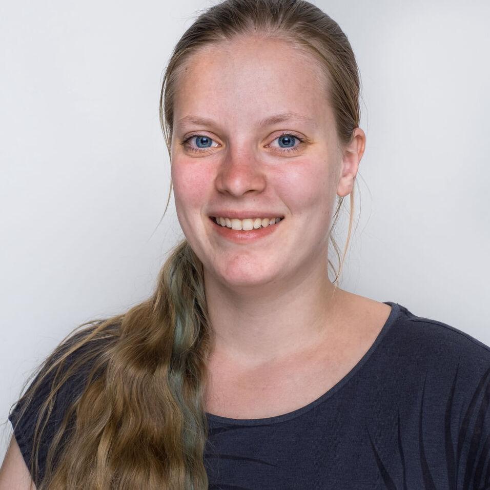 Lächelnde Frau mit langen, blonden Haaren und blauen Augen vor einem hellen Hintergrund.