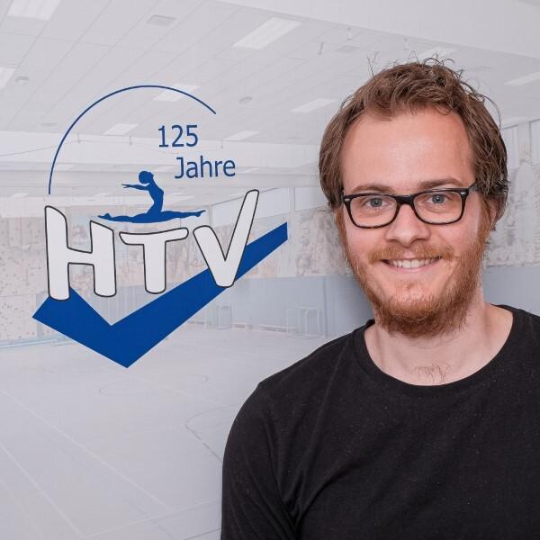 Mann mit Brille lächelt vor einem Hintergrund mit dem Logo des HTV und dem Schriftzug „125 Jahre“.
