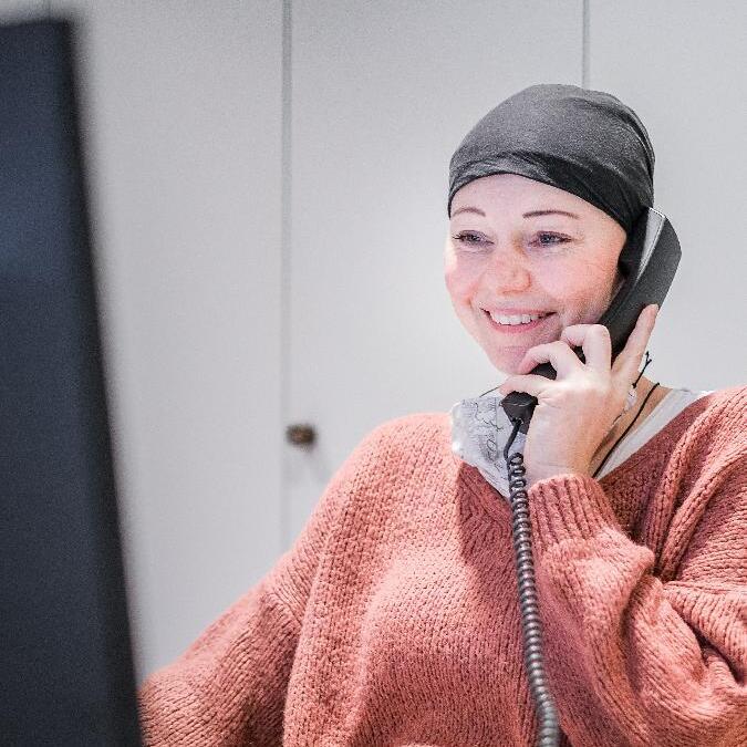 Frau mit Kopftuch lächelt am Telefon, sitzt an einem Schreibtisch mit Computer und Notizmappe.