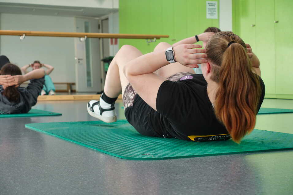 Gruppentraining: Menschen machen Sit-Ups auf gr&uuml;nen Matten in einem hellen, modernen Fitnessraum.