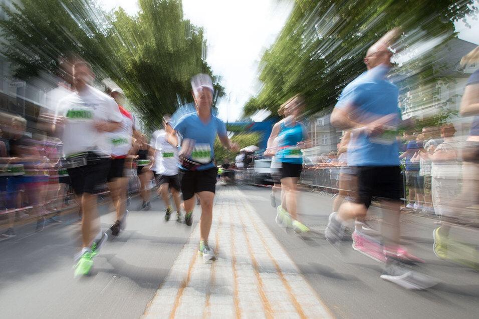 Schwenkaufnahme von laufenden Teilnehmern eines Straßenlaufes, umgeben von Zuschauern und grünen Bäumen.