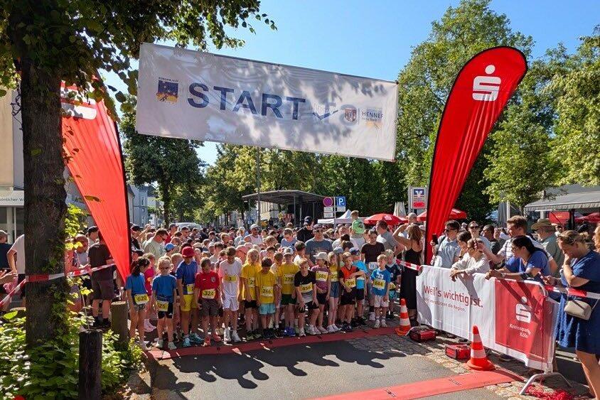 Startschuss für einen Kinderlauf mit vielen Teilnehmern, die an der Startlinie auf einer belebten Straße stehen.