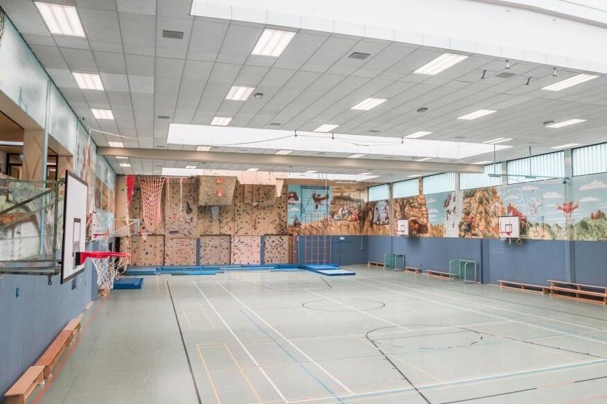 Luftaufnahme einer modernen Sporthalle mit Kletterwand, Basketballkorb und bunten Wandmalereien.