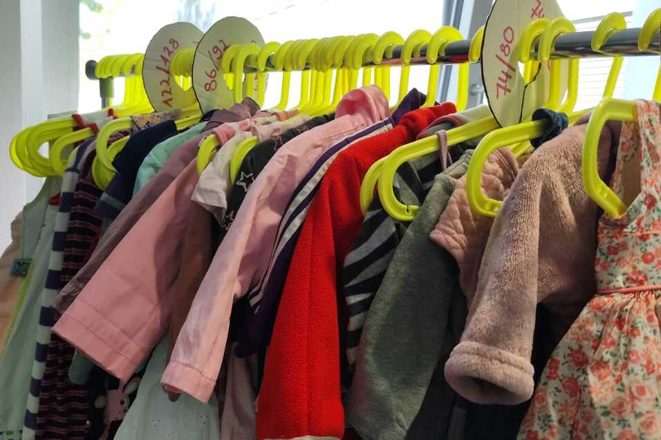 Bunte Kinderbekleidung h&auml;ngt an gelben Kleiderb&uuml;geln in einer Reihe.