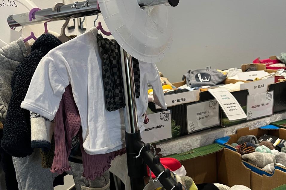 Kleiderst&auml;nder mit verschiedenen Kinderbekleidungsst&uuml;cken und Bekleidungsboxen in einem Verkaufsbereich.