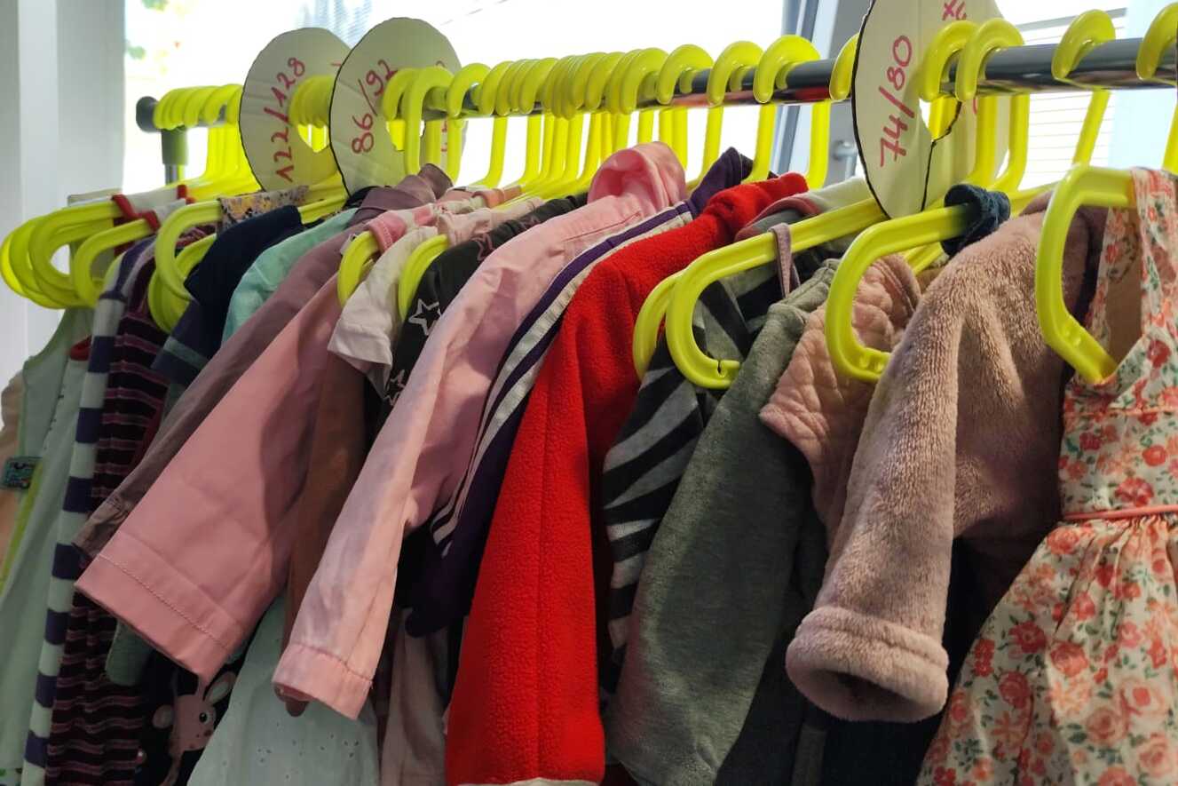 Bunte Kinderbekleidung h&auml;ngt an gelben Kleiderb&uuml;geln in einer Reihe.
