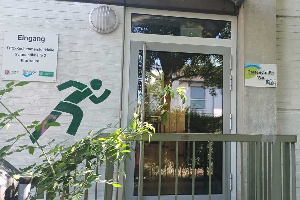 Eingang zu einer Sporteinrichtung, umrahmt von grünen Sportgrafiken: laufende und kletternde Figuren.