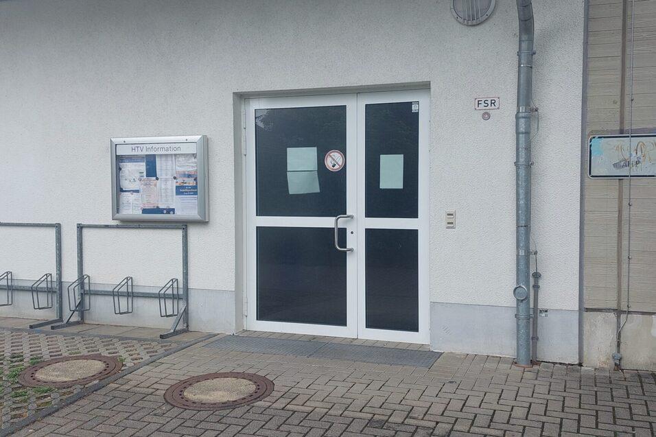Eingang zu einem Geb&auml;ude mit Glast&uuml;r, neben einem Informationskasten und Graffiti an der Wand.