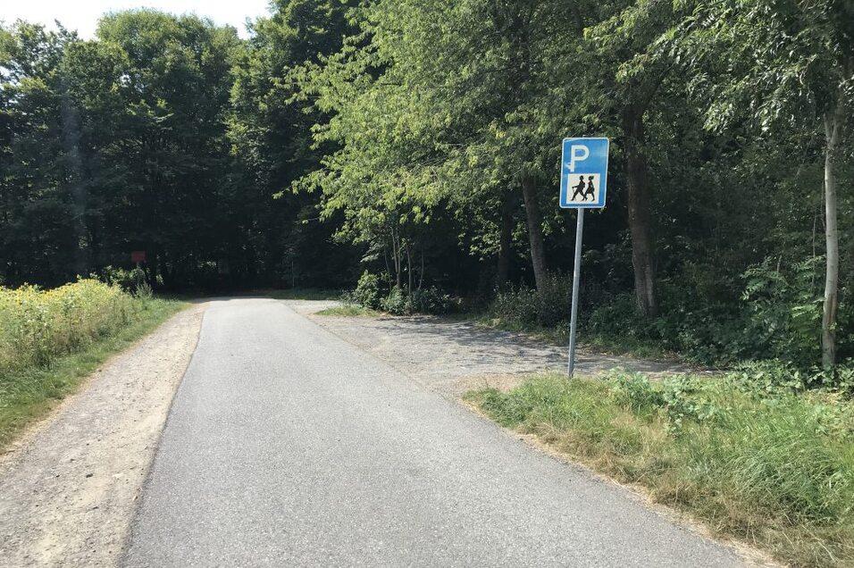 Wegweiser f&uuml;r Parkpl&auml;tze und Fu&szlig;g&auml;nger an einem schmalen Weg durch einen bewaldeten Bereich.
