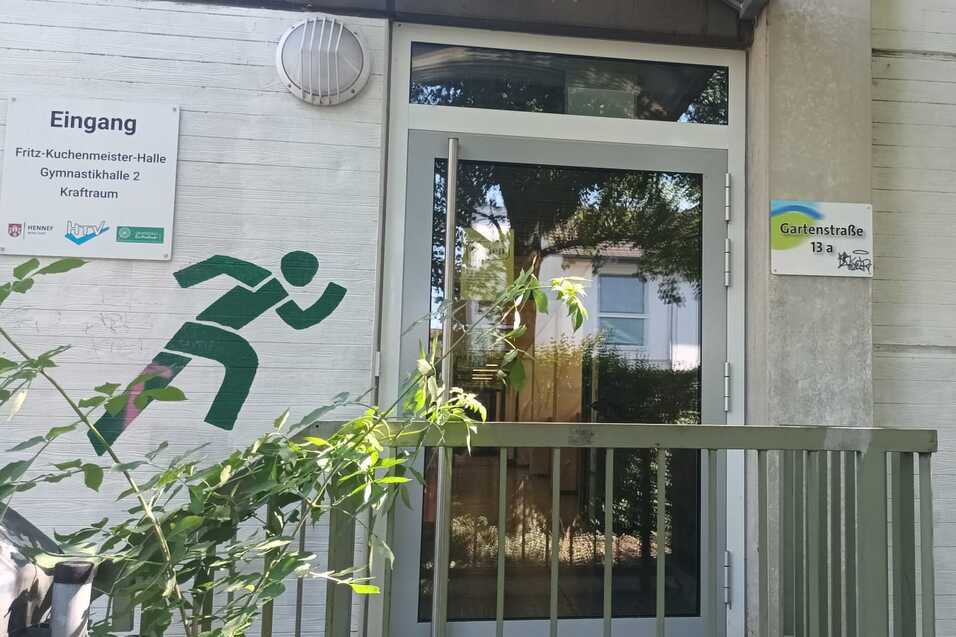 Eingang zu einer Sporteinrichtung, umrahmt von gr&uuml;nen Sportgrafiken: laufende und kletternde Figuren.