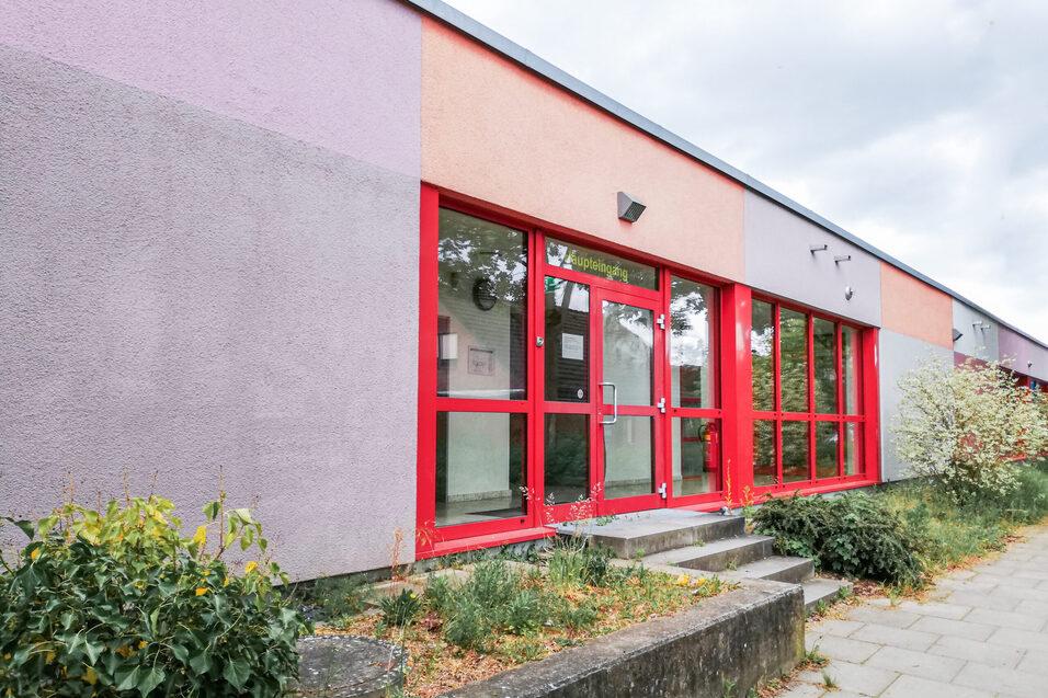 Fassade eines farbenfrohen Gebäudes mit roten Fenstern und einer StaTreppenanlage, umgeben von Pflanzen.