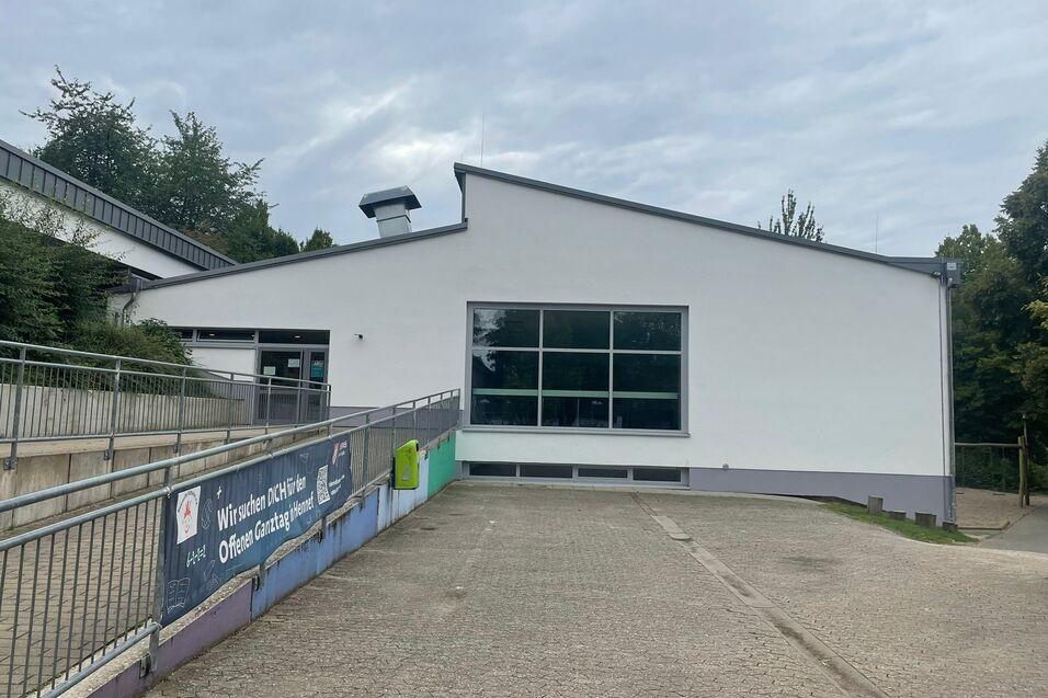 Moderne, einseitig belichtete Geb&auml;udeansicht mit gro&szlig;en Fenstern und Zugang zu einem gepflasterten Parkplatz.