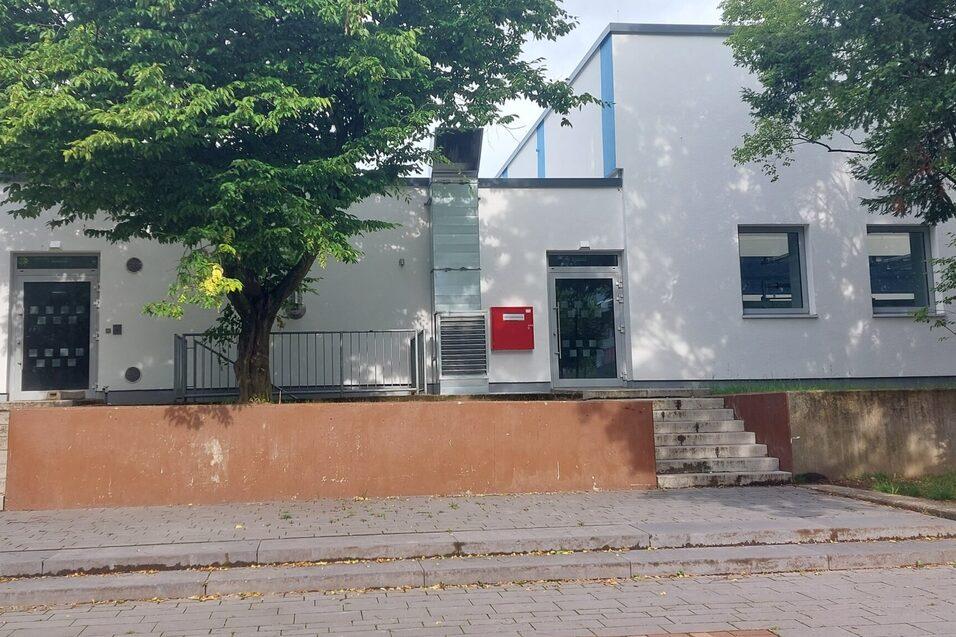 Eingangsbereich eines modernen, wei&szlig;en Geb&auml;udes mit Treppe, Gr&uuml;nfl&auml;chen und Postkasten an der Wand.