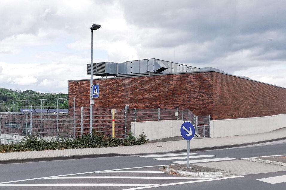Moderne Backsteinarchitektur eines Geb&auml;udes an einer Stra&szlig;e, umgeben von einer Zaun und B&auml;umen im Hintergrund.