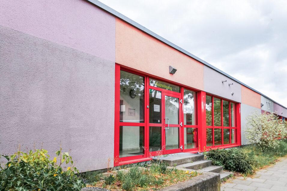 Fassade eines farbenfrohen Geb&auml;udes mit roten Fenstern und einer StaTreppenanlage, umgeben von Pflanzen.