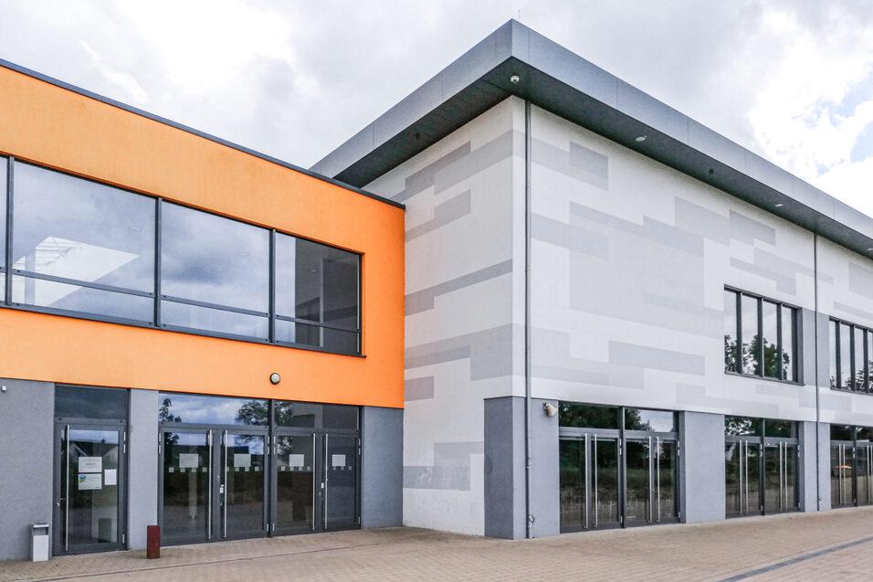 Moderne Geb&auml;udeansicht mit orangefarbenem und grauem Fassadenelement, gro&szlig;en Fenstern und Eingangst&uuml;ren.