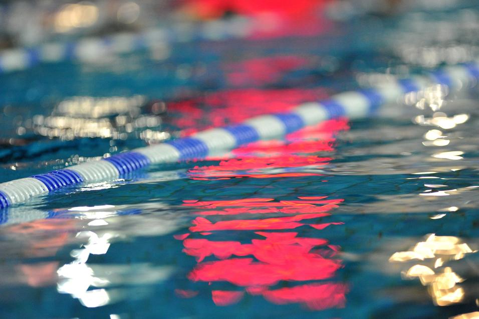 Reflektion einer blauen und weißen Schwimmbahn in klarem Wasser mit unscharfen Lichtern im Hintergrund.