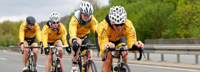 Vier Triathleten in gelben Jacken fahren in Gruppe mit Rennrädern